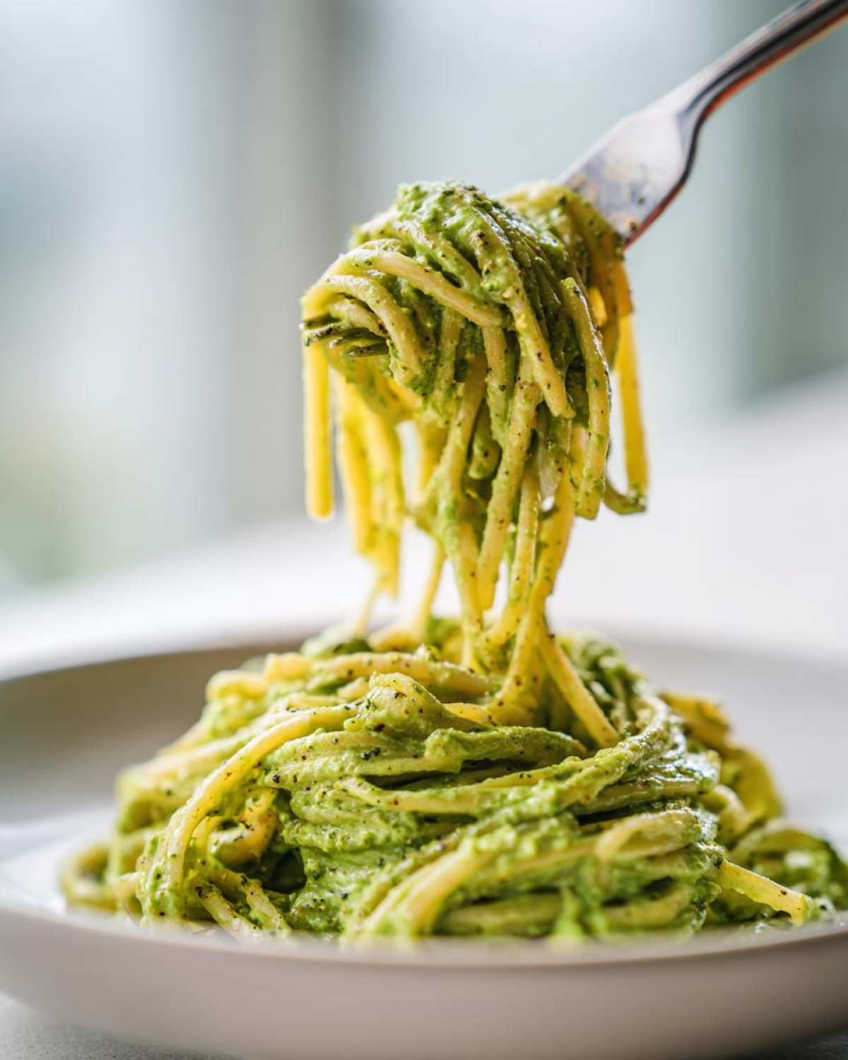 A fork lifting spaghetti coated in a thick, creamy green sauce, likely the Smoky Poblano Cream Sauce, from a white plate.