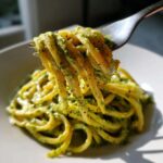 A fork lifts thick strands of pasta coated in a creamy green sauce, likely the Smoky Poblano Cream Sauce.