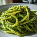 Close-up of thick pasta noodles coated in a vibrant green Smoky Poblano Cream Sauce, served on a white plate.