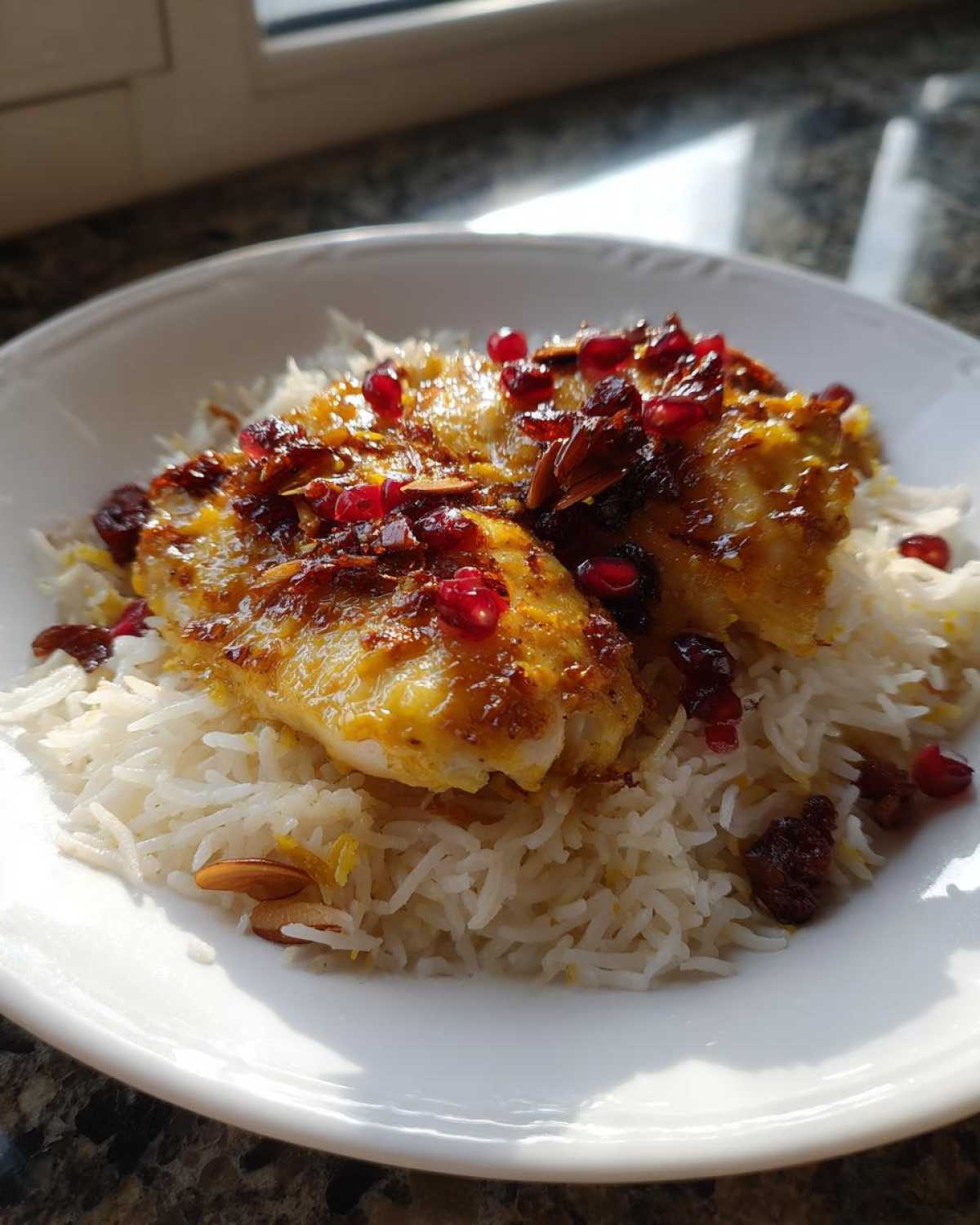 Close-up of a serving of Persian Chicken over fluffy saffron rice, topped with bright pomegranate seeds and slivered almonds.