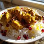 A plate of golden Persian Chicken stew served over fluffy saffron rice, garnished with pomegranate seeds and slivered almonds.