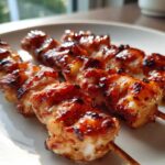 Close-up of three glossy, grilled Pineapple Teriyaki Chicken Skewers resting on a white plate.