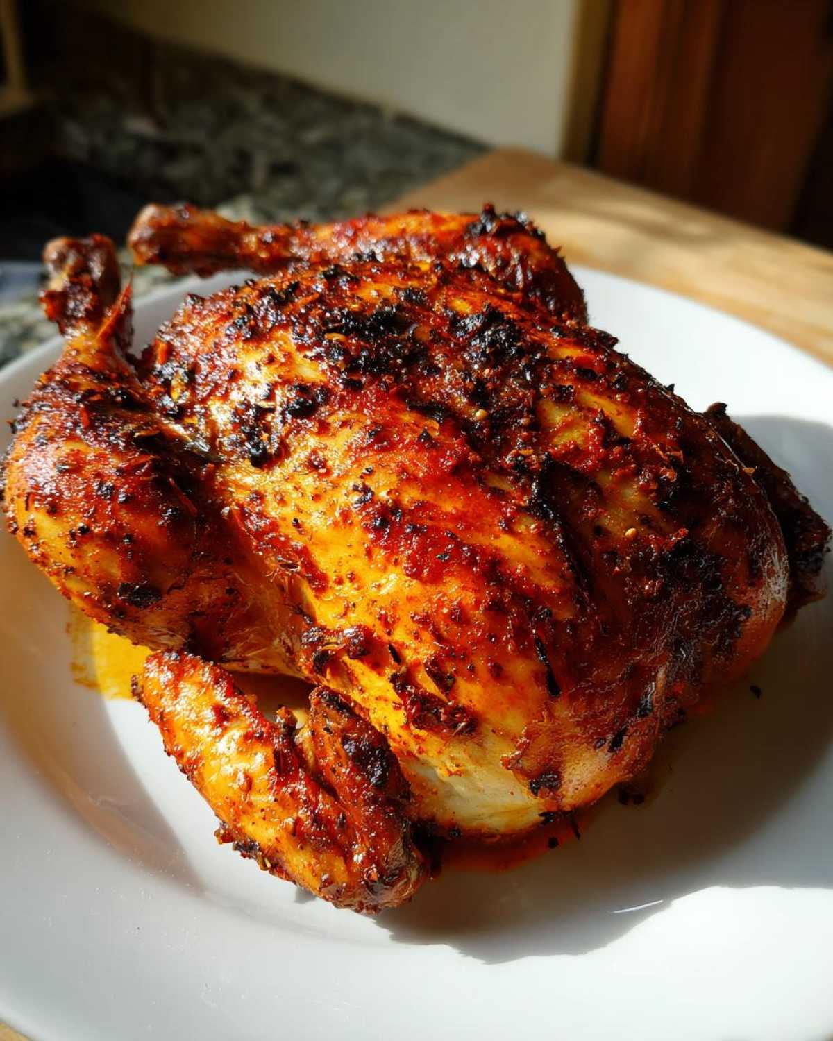 A whole, beautifully roasted Pollo Asado with crispy, dark red-orange seasoned skin resting on a white plate.