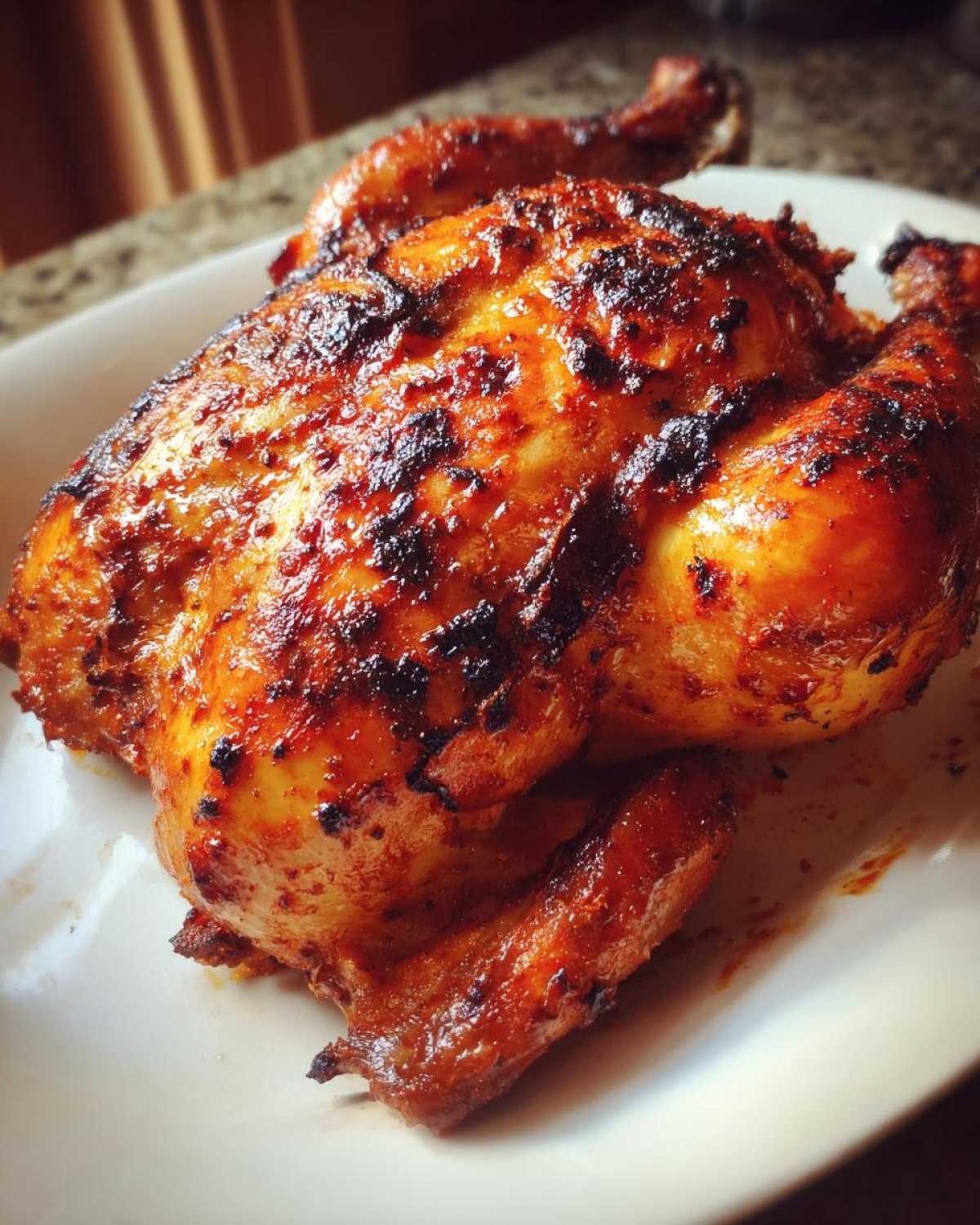 Close-up of a whole, juicy Pollo Asado Mexican grilled or roasted chicken with deeply charred, reddish-orange skin.