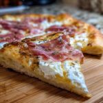 Close-up of a slice of Prosciutto Honey Burrata Pizza showing thick crust, creamy burrata, prosciutto, and a honey drizzle.