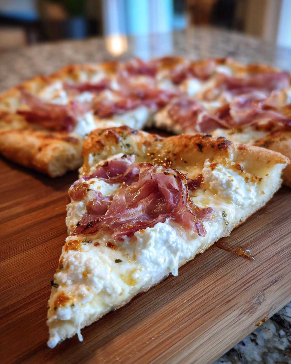 Close-up of a slice of Prosciutto Honey Burrata Pizza featuring creamy burrata and prosciutto on a wooden board.
