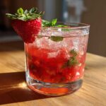 A close-up of a Refreshing Strawberry Basil Smash Cocktail garnished with a fresh strawberry and mint leaves.