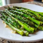 Close-up of bright green Sautéed Garlic Butter Asparagus Skillet spears glistening with butter and minced garlic on a white plate.