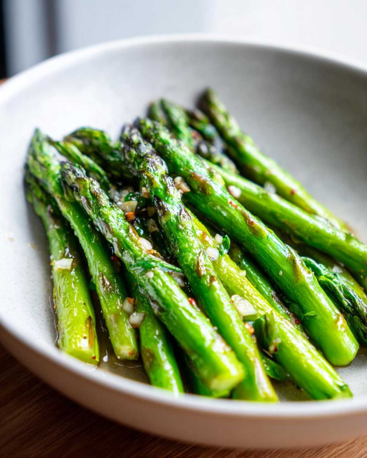 Close-up of bright green Sautéed Garlic Butter Asparagus Skillet spears glistening with butter and minced garlic in a light bowl.