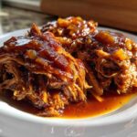 Close-up of shredded Hawaiian Chicken smothered in a rich, glossy, dark brown sauce on a white plate.