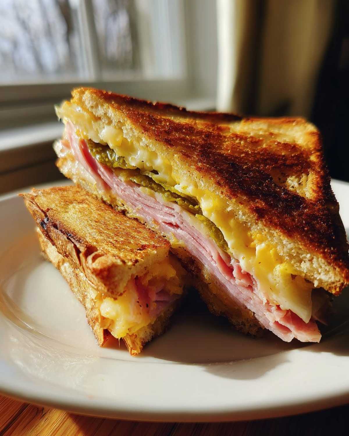 A cross-section of a Sizzling Cuban Grilled Cheese showing melted cheese, ham, and pickles between golden, toasted bread.