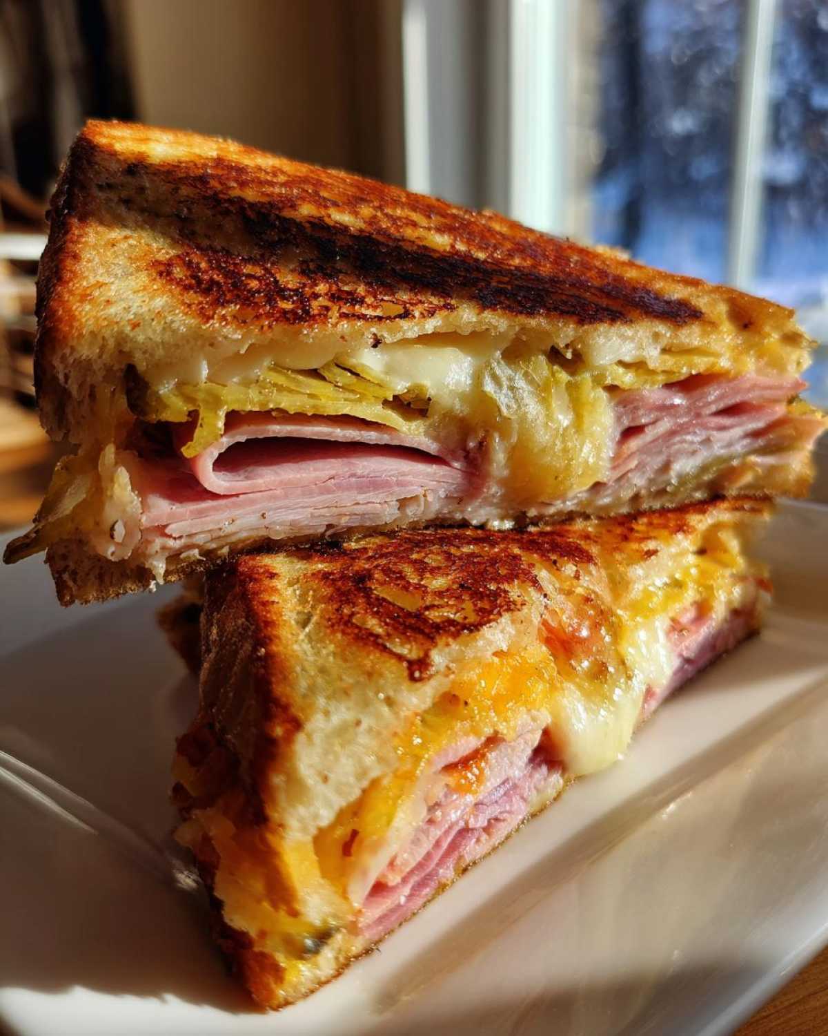 Close-up of a Sizzling Cuban Grilled Cheese cut in half, showing melted cheese, ham, and pickles inside.