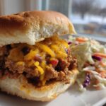 A close-up of a cheesy sloppy joe slider served with a side of coleslaw, perfect for a cookout spread.