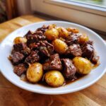 A white plate filled with tender chunks of Slow Cooker Garlic Butter Beef with Potatoes, coated in a rich brown sauce.