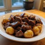 A white bowl filled with chunks of Slow Cooker Garlic Butter Beef with Potatoes, glistening in sauce.