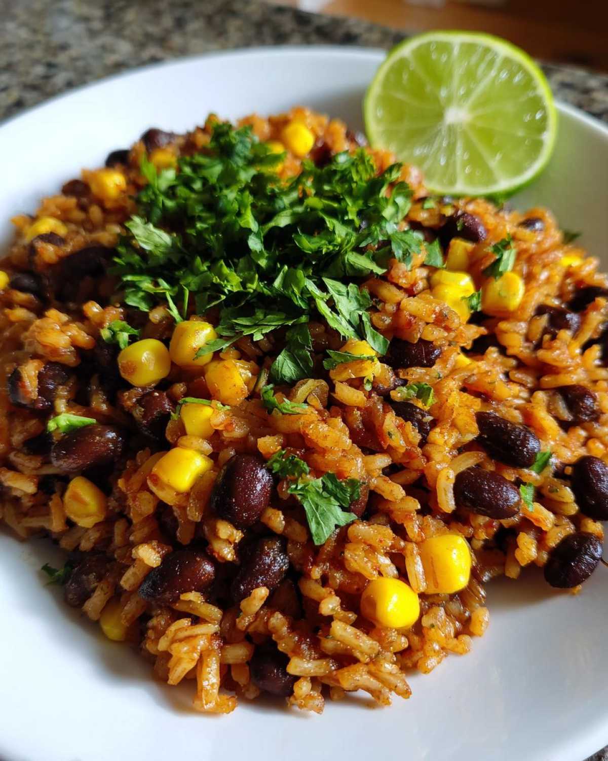A close-up of a bowl of Southwest Beans and Rice One Pot Weeknight Dinner, topped with fresh cilantro and a lime wedge.