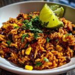 A close-up of flavorful Southwest Beans and Rice in a white bowl, garnished with fresh cilantro and lime wedges.