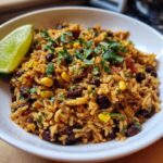 A white bowl filled with flavorful Southwest Beans and Rice, garnished with cilantro and a lime wedge.