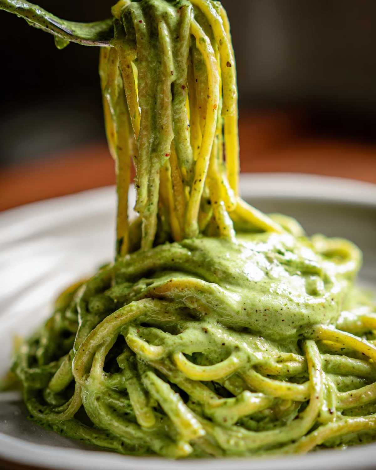 Close-up of spaghetti being lifted, heavily coated in vibrant green Smoky Poblano Cream Sauce.