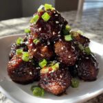 A mound of glazed Sticky Hoisin Meatballs Asian Cuisine Appetizer garnished with sesame seeds and green onions.