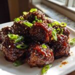 Close-up of glistening Sticky Hoisin Meatballs Asian Appetizer piled on a white plate, garnished with sesame seeds and green onions.