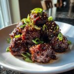 A stack of glazed Sticky Hoisin Meatballs Asian Appetizer, garnished with sesame seeds and sliced green onions.