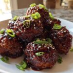 A pile of glazed Sticky Hoisin Meatballs Asian Cuisine Appetizer garnished with sesame seeds and sliced green onions.