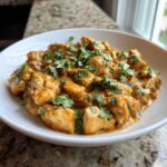 Close-up of tender chicken pieces coated in rich sauce, served in a white bowl, garnished with fresh cilantro for Thai Spiced Peanut Butter Chicken.