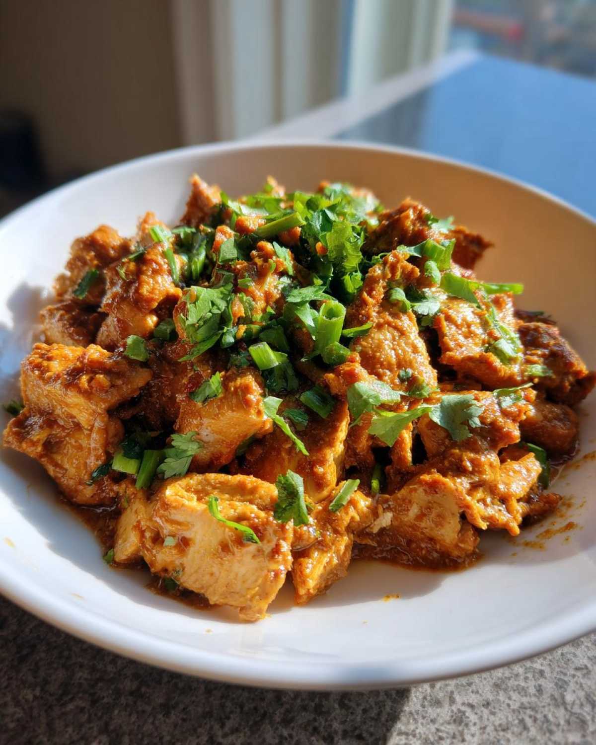 Close-up of diced chicken coated in a rich sauce, served in a white bowl, garnished with fresh cilantro for Thai Spiced Peanut Butter Chicken.