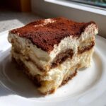A delicious slice of Tiramisu, layered with cream and coffee-soaked ladyfingers, dusted with cocoa powder, relating to Recetas de Café.