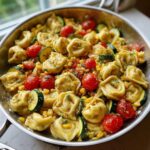Close-up of Tortellini with Summer Vegetables, including zucchini, corn, and cherry tomatoes, tossed in a light sauce in a stainless steel skillet.
