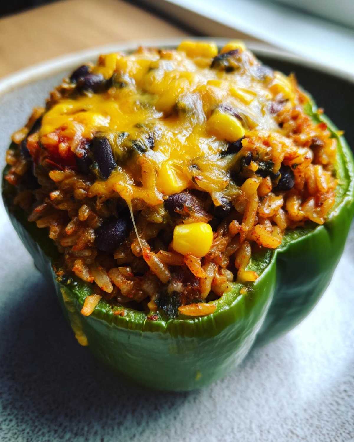 Close-up of a green bell pepper stuffed with seasoned rice, black beans, corn, and melted cheddar cheese, perfect for Vegetarian Stuffed Peppers Rice.