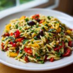 Close-up of a vibrant Veggie Rainbow Orzo Salad featuring orzo pasta, red and yellow peppers, olives, and fresh parsley.